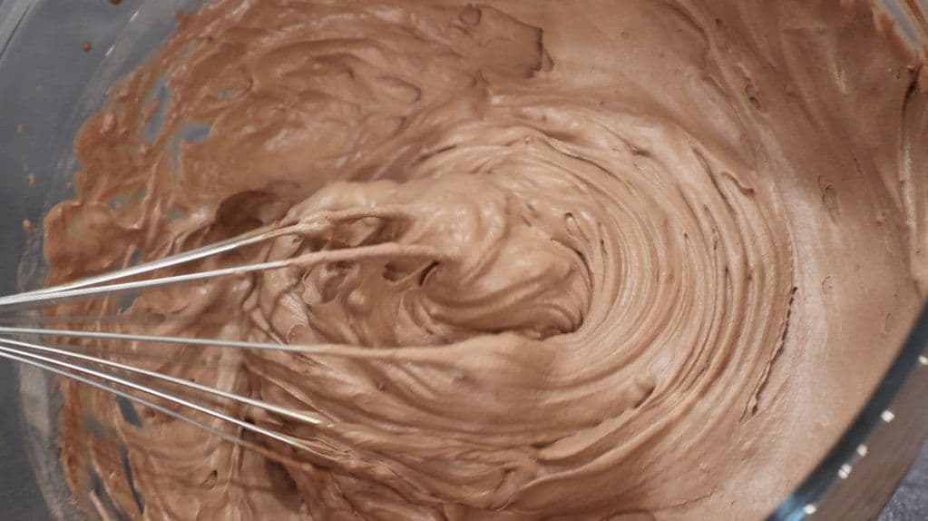 Chocolate whipped cream being whisked with a whisk in a bowl, showing soft peaks texture.
