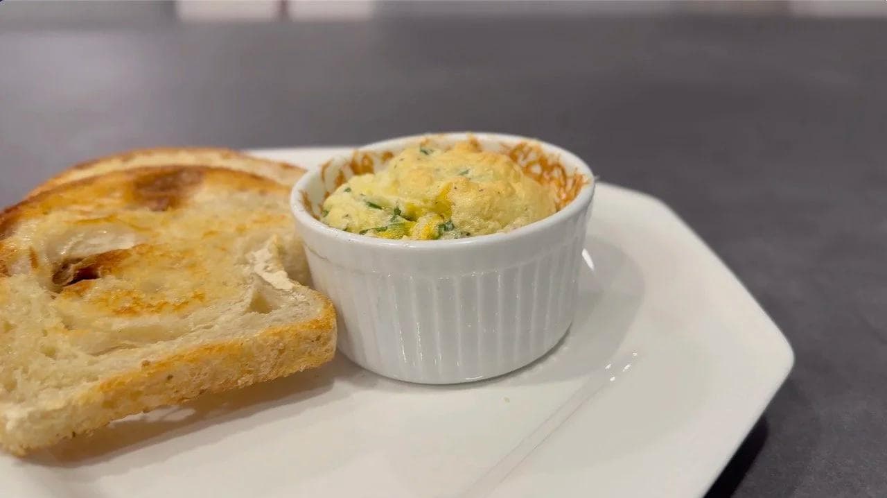 Cheesy egg souffle in a white ramekin served alongside toasted bread on a white plate.
