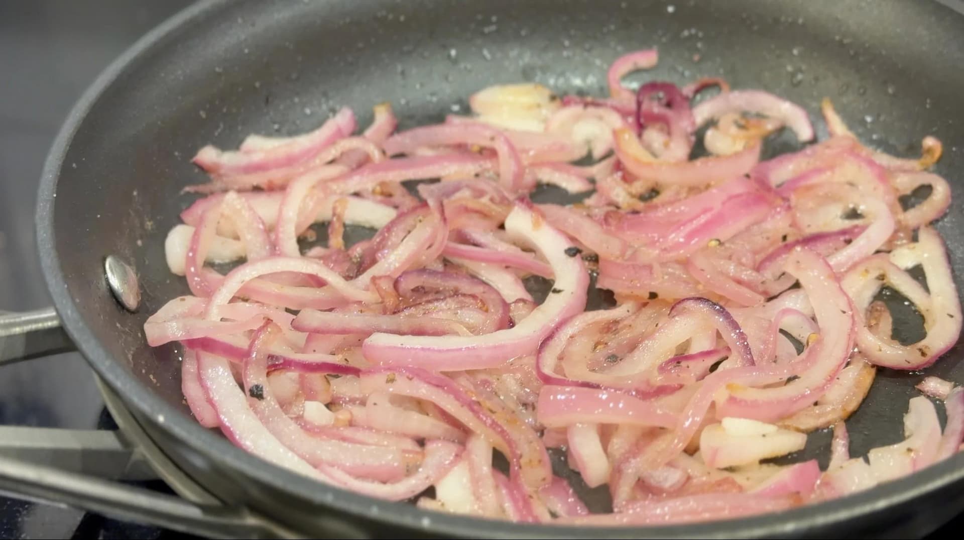 Sliced red onions cooking in a cast iron skillet with oil, showing browning at the edges.