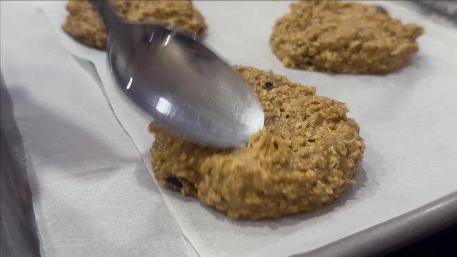 Flattening pumpkin chocolate chip cookie dough with the back of a spoon on parchment paper.