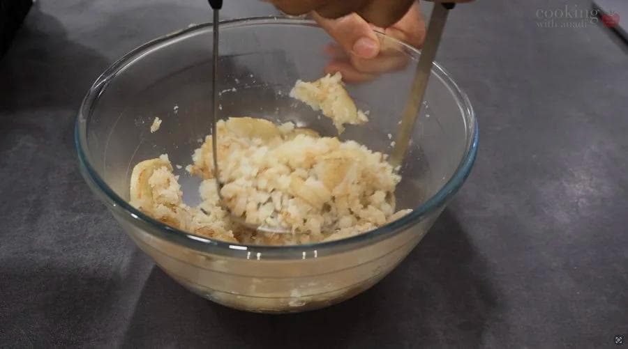 Mashed potatoes being mixed with a wooden spoon in a glass bowl during perkedel preparation.