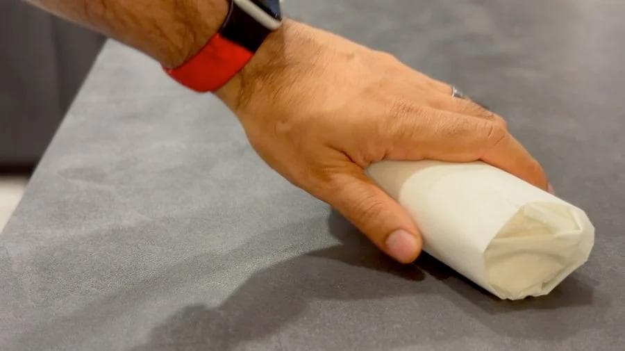 Hand wrapping a breakfast burrito in parchment paper on a gray surface for freezing.