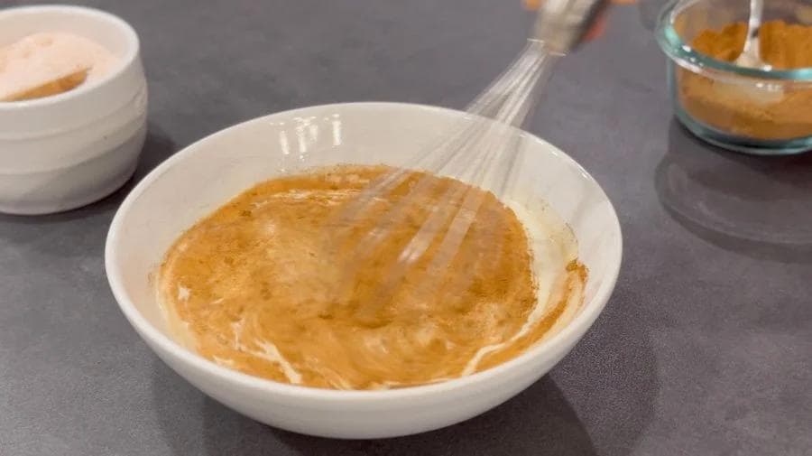 Whisked pumpkin egg mixture in a white bowl with a whisk, ready to be tempered for pumpkin rice pudding.