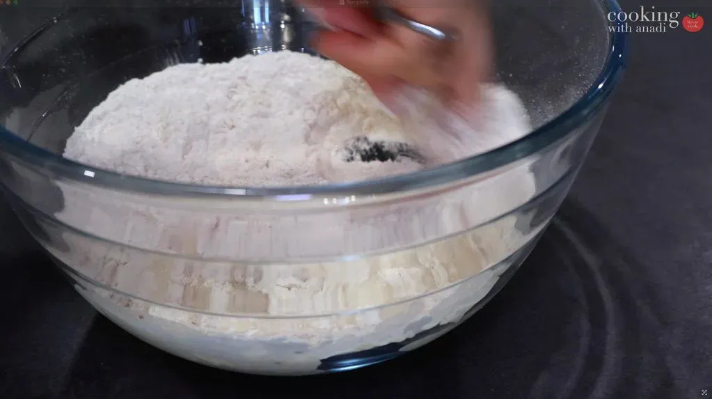 Kneading poori dough in a glass bowl with flour, ajwain seeds, and water mixed together