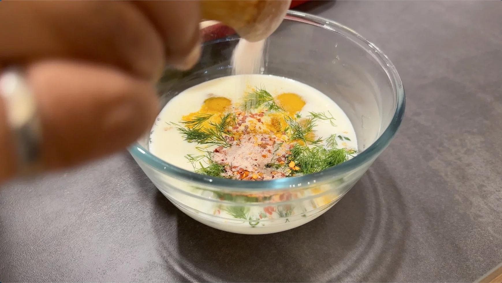 Egg mixture with dill, spices, and mustard being poured into a glass bowl for French toast preparation.