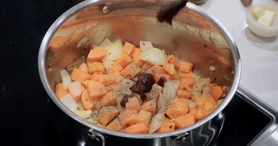 Pot of diced carrots, onions, and potatoes with black pepper and seasoning mixed in before adding water.