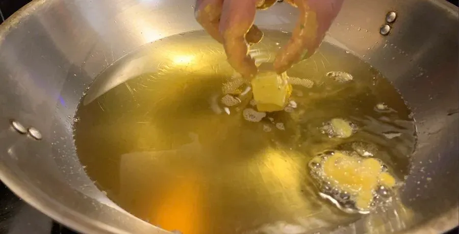Paneer pakora being dropped into hot golden oil in a stainless steel pan during frying.