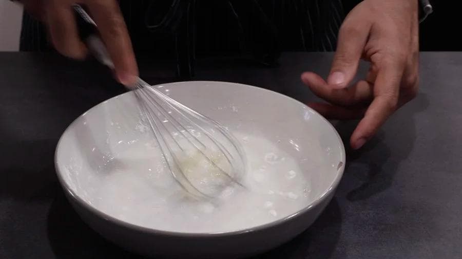 Whisking wet batter in a white bowl with a wire whisk during chicken nugget preparation.