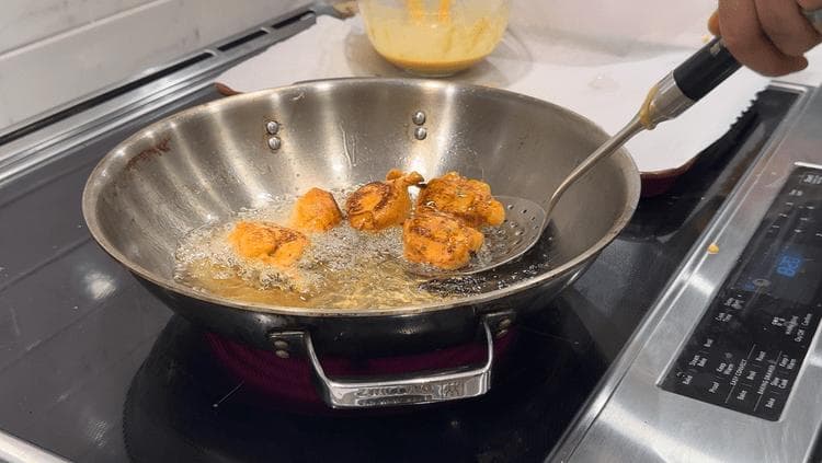Golden paneer pakoras frying in oil in a wok on an induction cooktop.