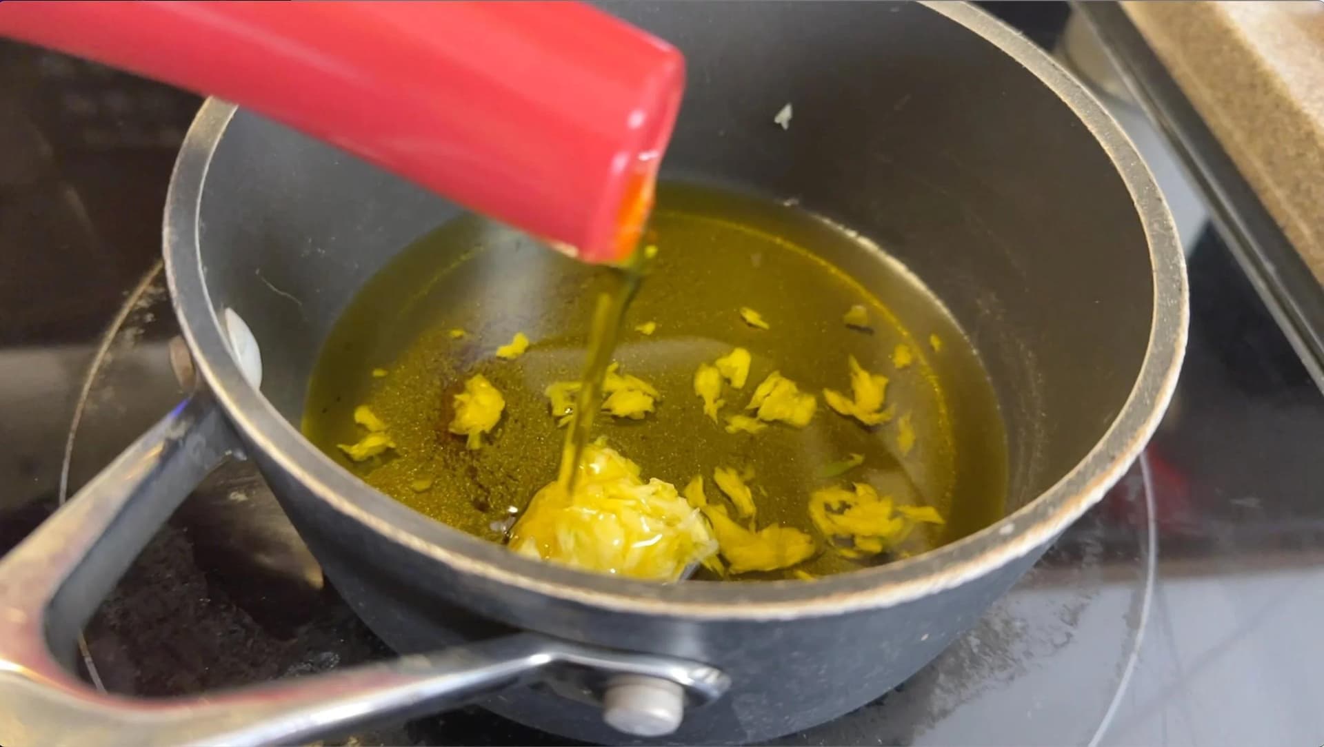 Olive oil being poured into a saucepan with chopped garlic cloves on medium-low heat.