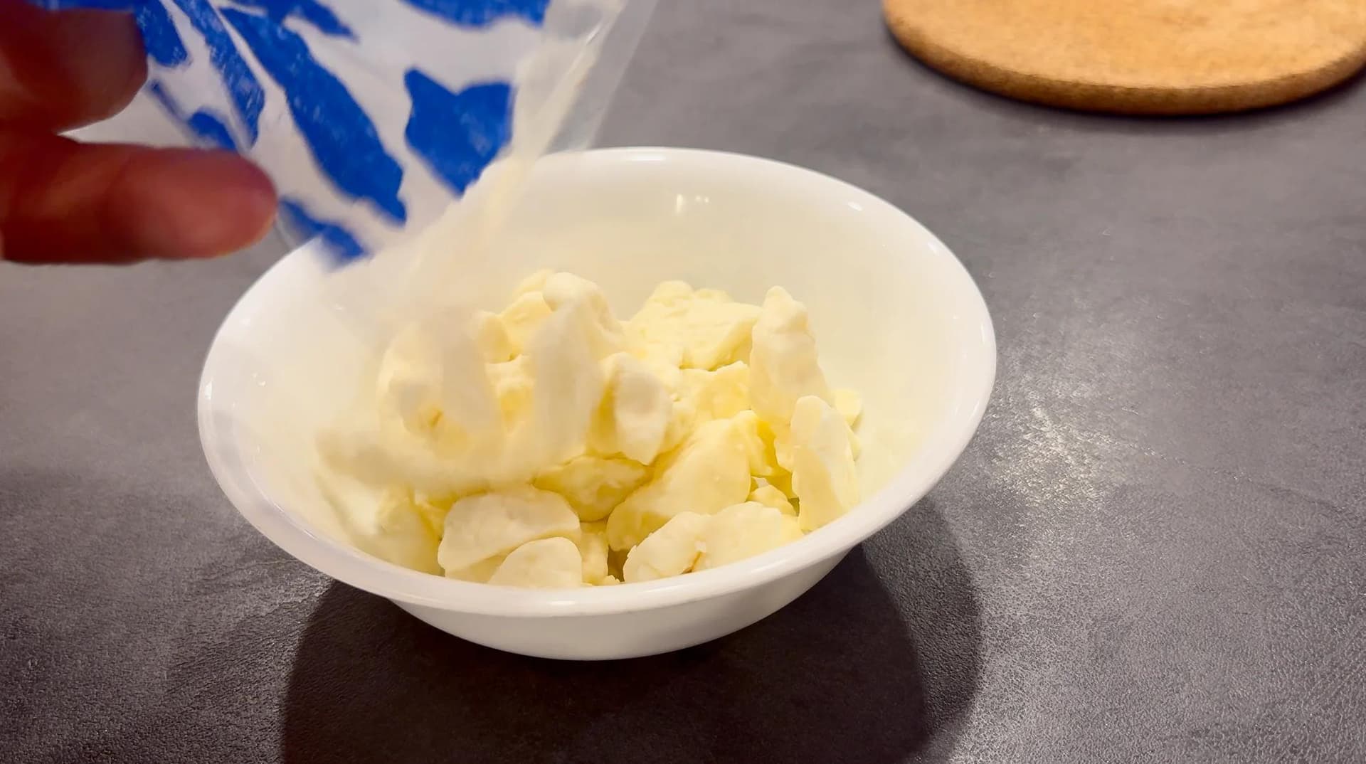 White bowl filled with fresh cheese curds on a gray countertop during poutine assembly.