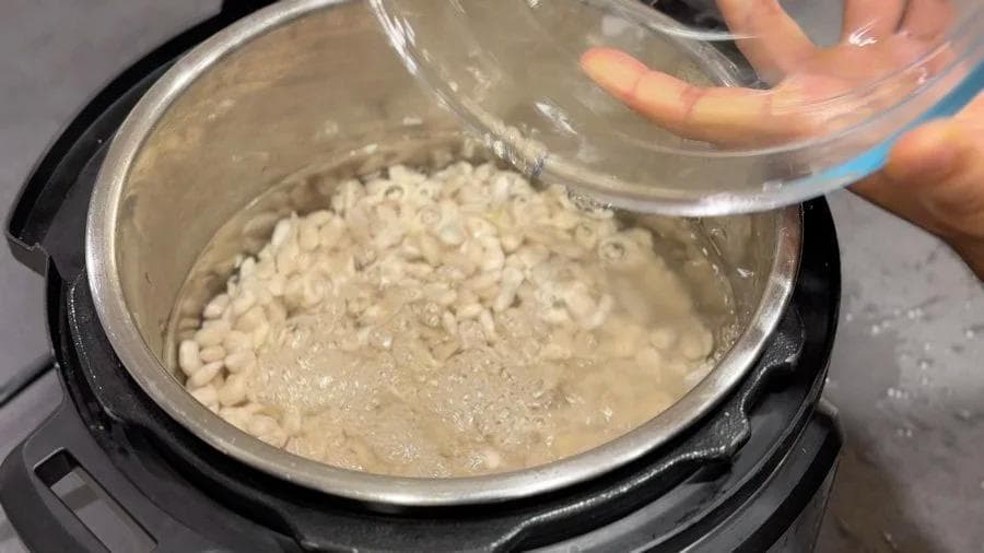 Water being poured into an Instant Pot containing rinsed white beans for cooking.