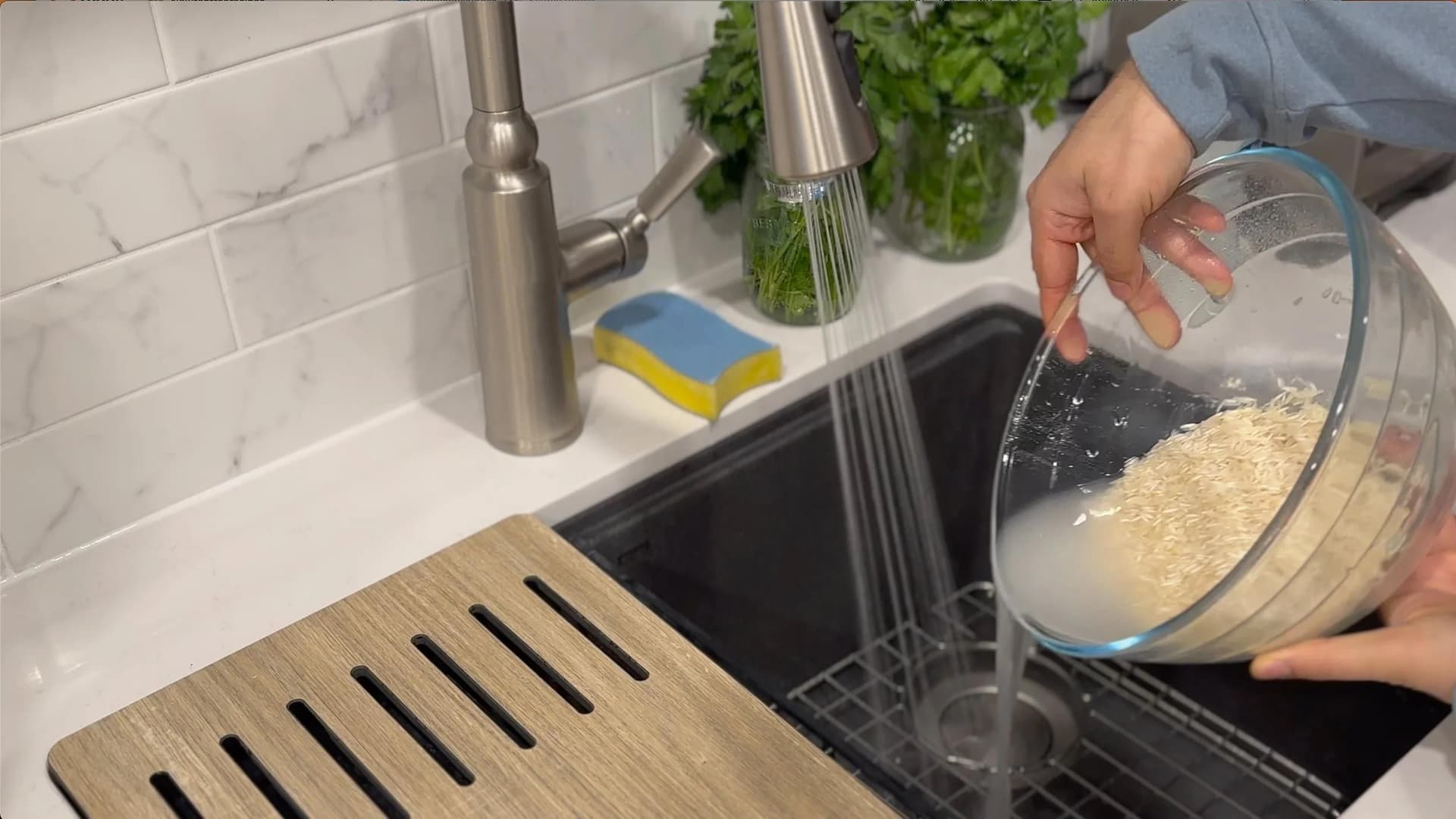 Rinsing rice in a clear bowl over a black kitchen sink with a stainless steel faucet visible
