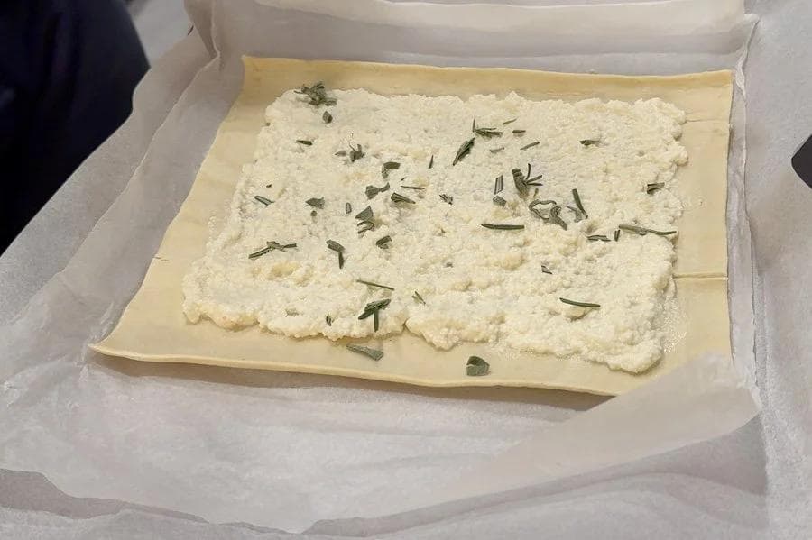 Ricotta mixture spread on puff pastry with fresh herbs sprinkled on top, ready for folding.