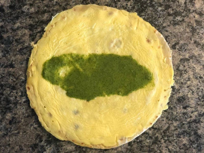 Cooked paratha with green cilantro-mint chutney spread in the center on a granite surface.
