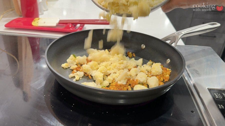Cooked potatoes and onions being added to a pan with spices during preparation of aloo patty filling.