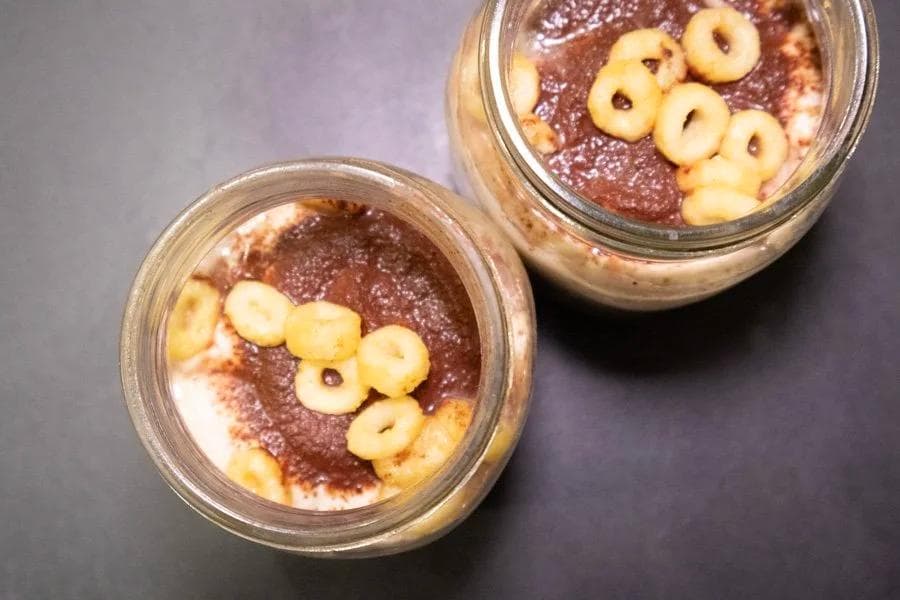 Two glass jars of tiramisu overnight oats topped with whipped cream, cocoa powder, and cereal rings.