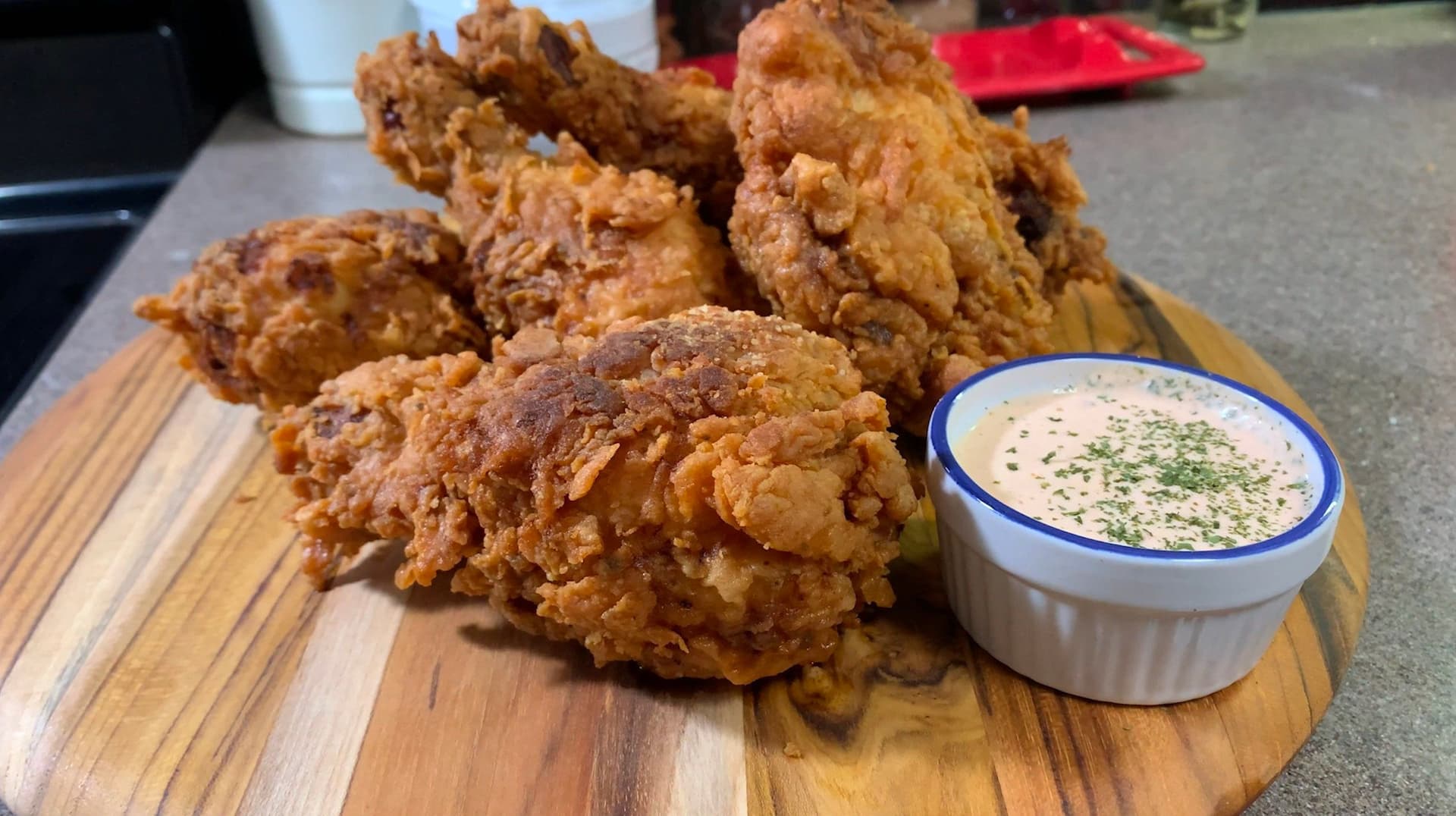 Golden crispy buttermilk fried chicken pieces on a wooden board with herb aioli dipping sauce.