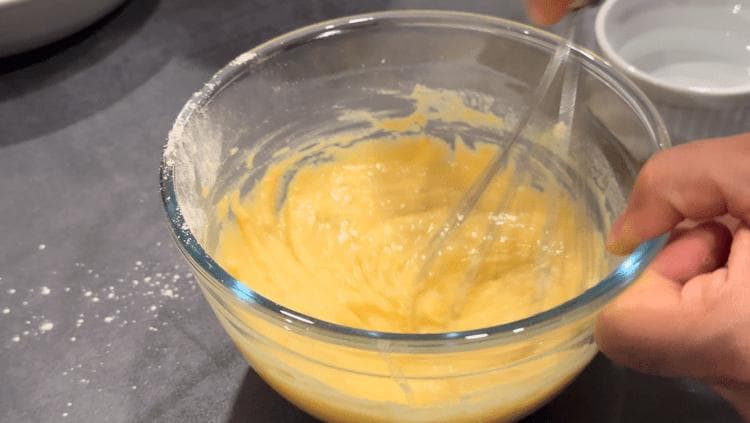 Thick golden besan batter in a glass bowl, whisked to smooth consistency for paneer pakora.