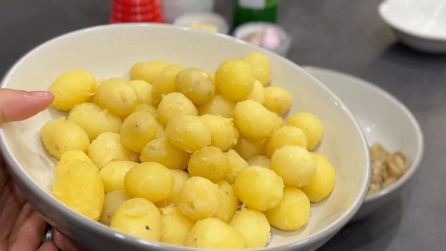 Peeled yellow baby potatoes in a white bowl held in hand, ready for sautéing.