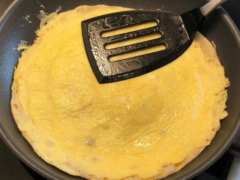 Cooked scrambled eggs on paratha in a dark pan, being pressed with a black spatula.