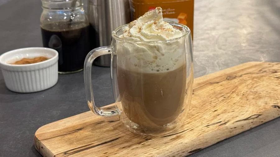 Iced gingerbread latte in a glass mug topped with whipped cream and spices, served on a wooden board.