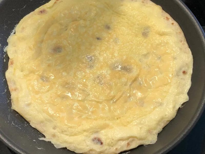 Cooked egg and paratha in a skillet being pressed with a spatula, showing golden-brown color with specks throughout.