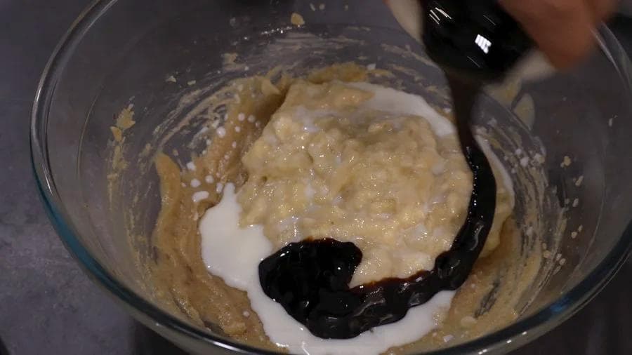 Mashed bananas, milk, and molasses being mixed into butter and sugar in a glass bowl.