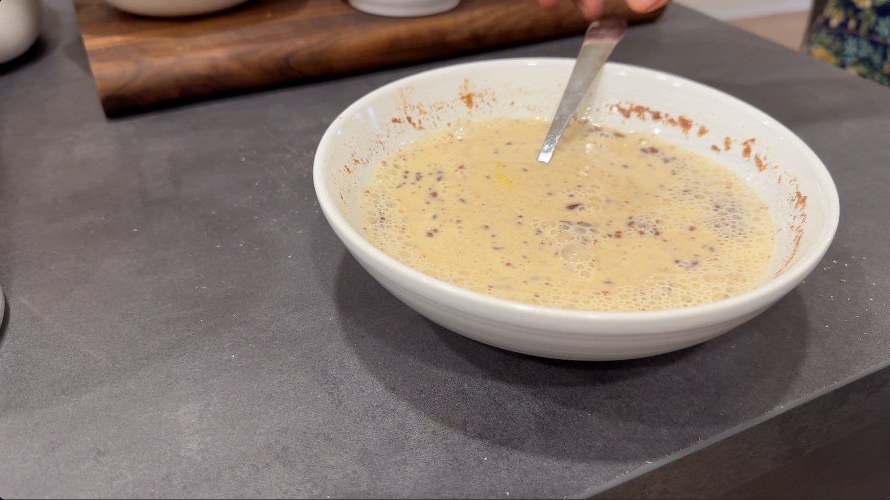 Whisked egg mixture with cinnamon and spices in a white bowl with a whisk, ready for French toast casserole.