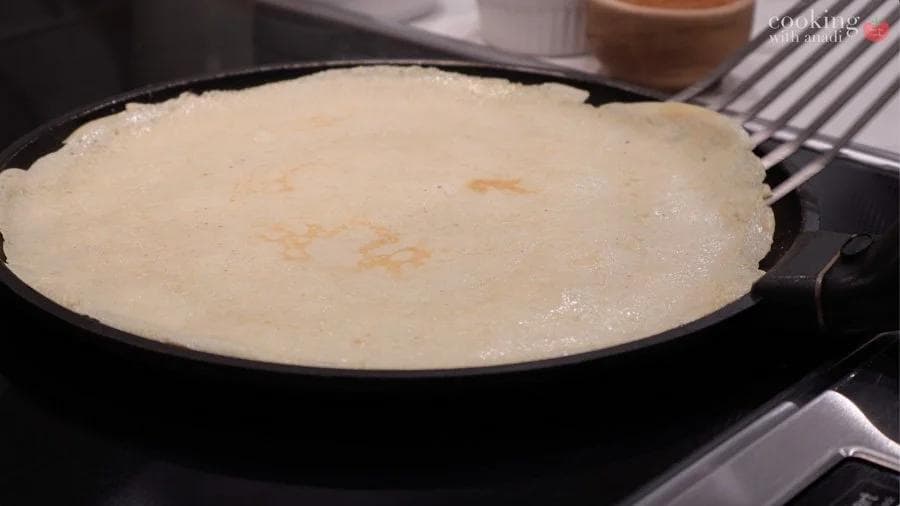 Crepe cooking in a non-stick pan, showing a thin, lightly golden crepe with melted butter.