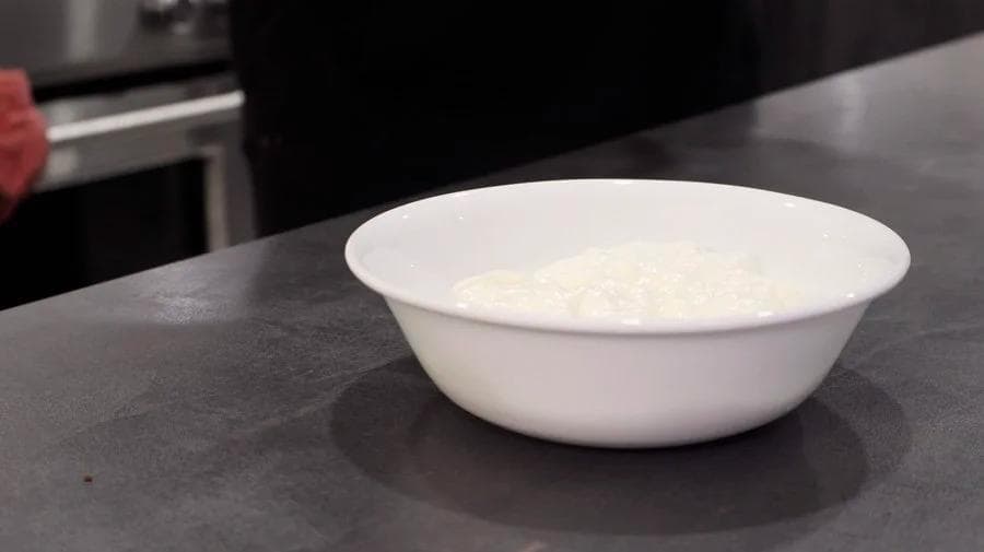 White bowl of yogurt mixture with vanilla and maple syrup topping for overnight oats on dark countertop.