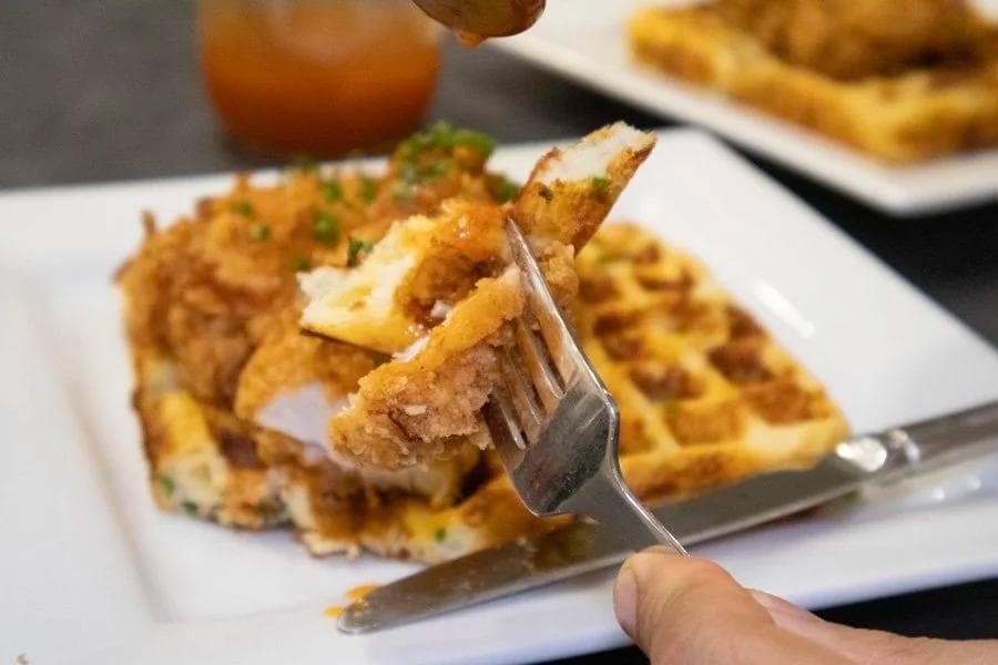 Crispy fried chicken piece on a waffle topped with hot honey, held on a fork over a white plate.