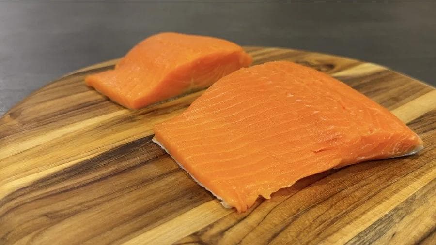 Two salmon fillets on a wooden cutting board, patted dry and ready for seasoning.