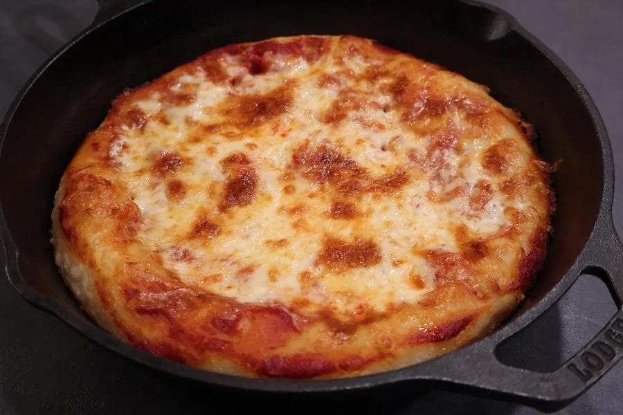 Golden-brown cast iron skillet pizza with melted cheese and crispy edges.
