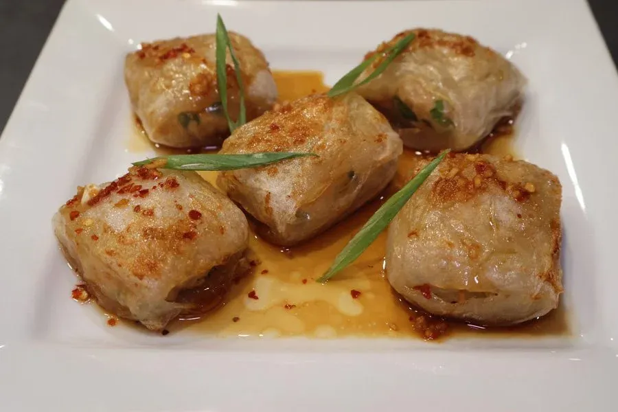 Four crispy rice paper chicken dumplings on a white plate with sauce and green onion garnish.