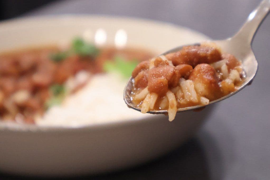 Spoonful of rajma masala with kidney beans and rice being held over a bowl of creamy curry.