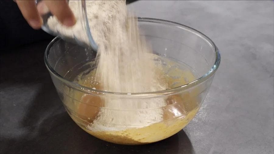 Flour being folded into a bowl of wet pumpkin cookie batter with chocolate chips.