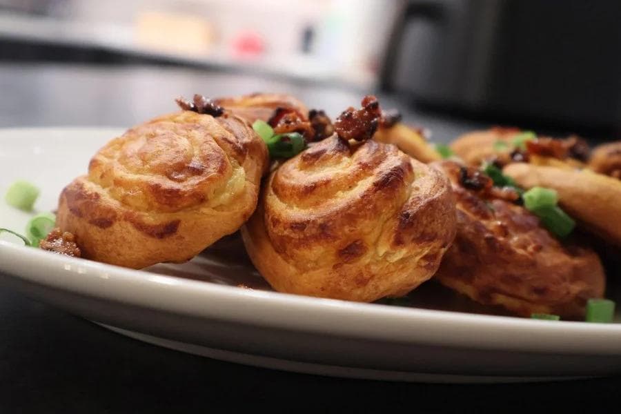 Air fryer mashed potato pinwheels garnished with green peas on a white plate.