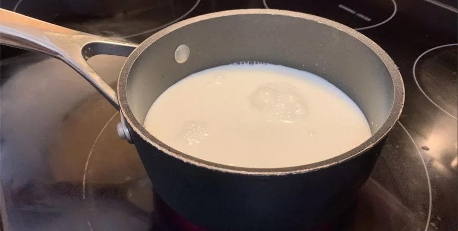 White chocolate mocha mixture warming in a dark pot on the stove, pale cream-colored liquid visible.