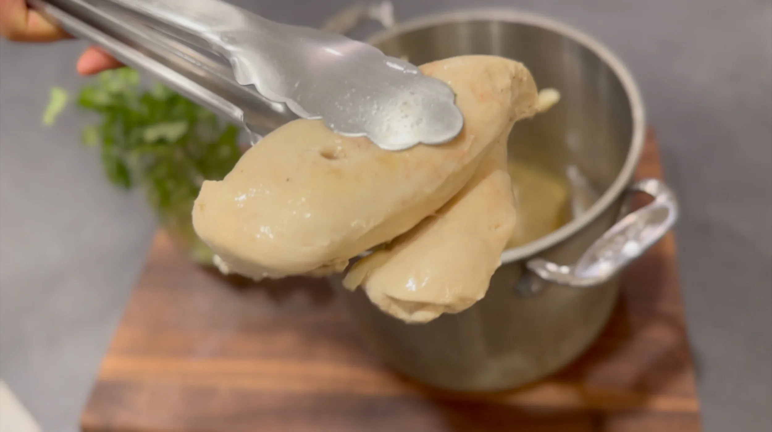 Sliced poached chicken breast being lifted with tongs from a pot of broth.