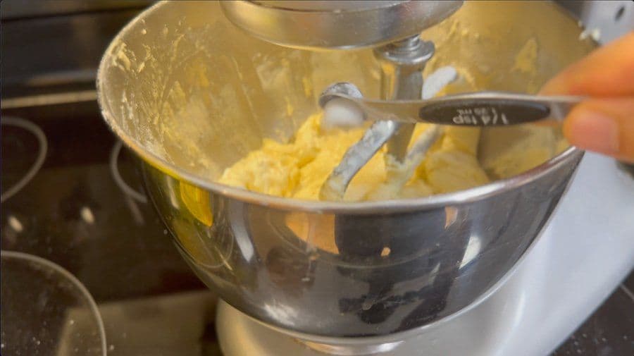 Electric mixer beating thick yellow cookie batter in stainless steel bowl with paddle attachment.