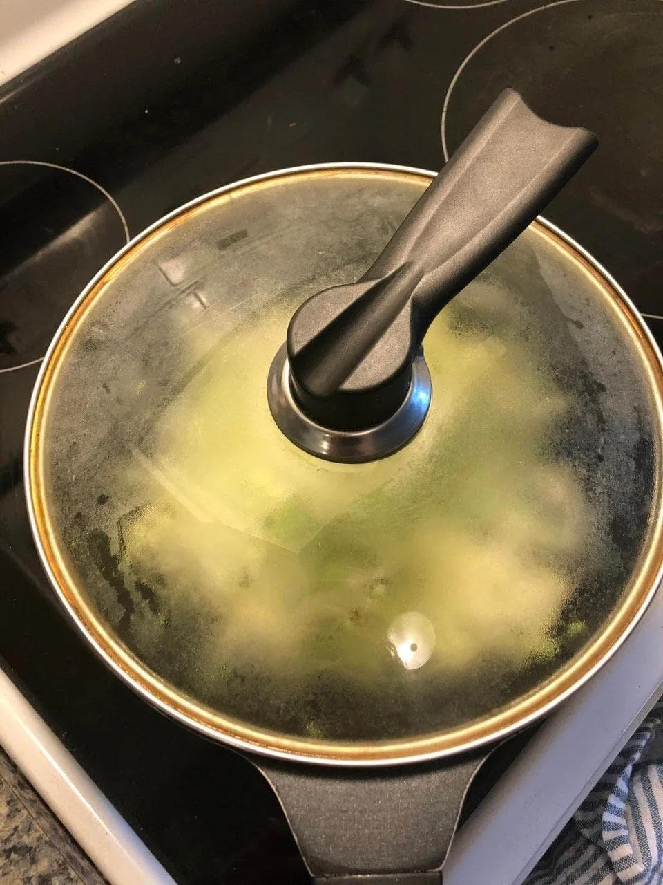 Covered wok with shredded cabbage cooking in oil on stovetop, mid-preparation.