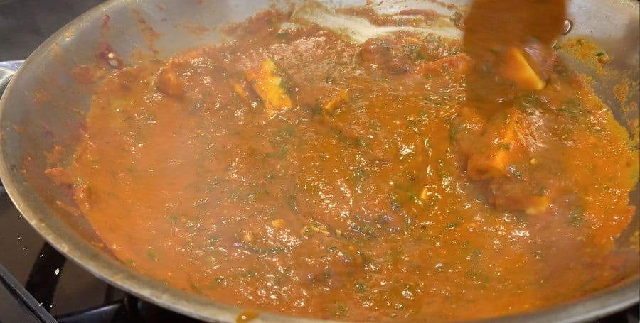 Simmering ginger-cilantro paneer gravy in a pan with rich orange-brown sauce and visible spices.