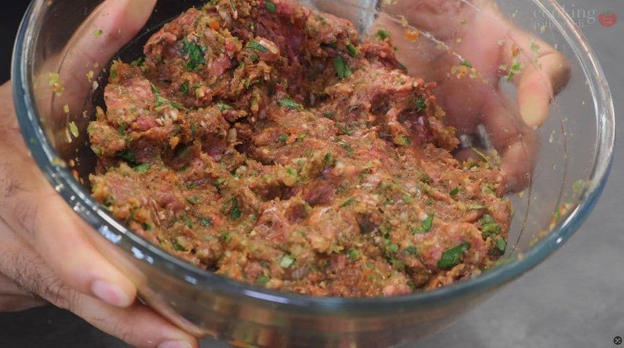 Meat and vegetable mixture with parsley and spices in a glass bowl, held in hands during preparation.