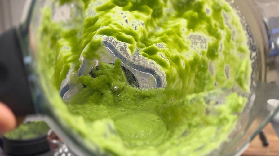 Bright green amla chutney being blended in a food processor to a smooth, puréed consistency.
