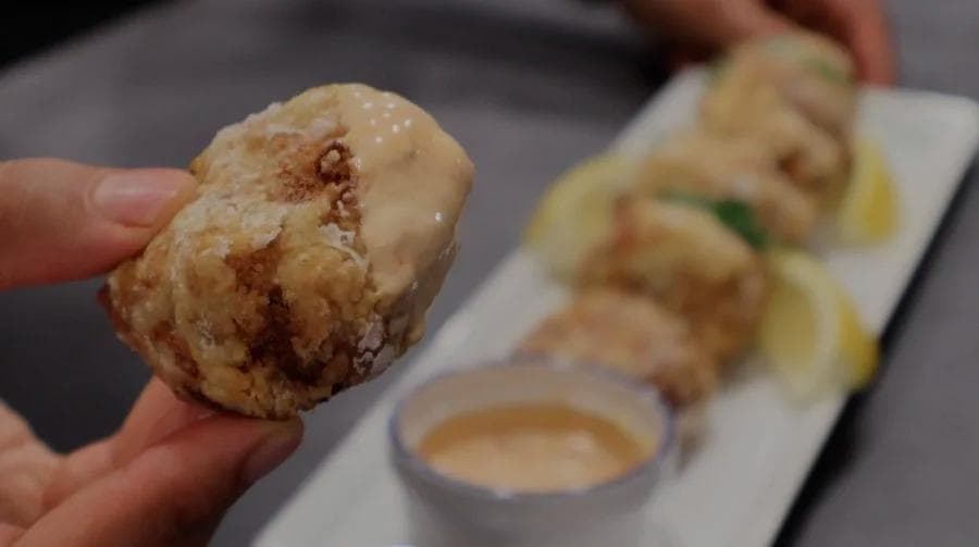 Golden brown perkedel potato fritter held in hand with dipping sauce and more fritters on plate in background