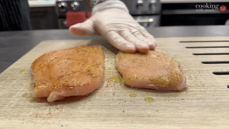 Two seasoned chicken breasts on a wooden cutting board, one with salt and pepper, one with blackening seasoning.