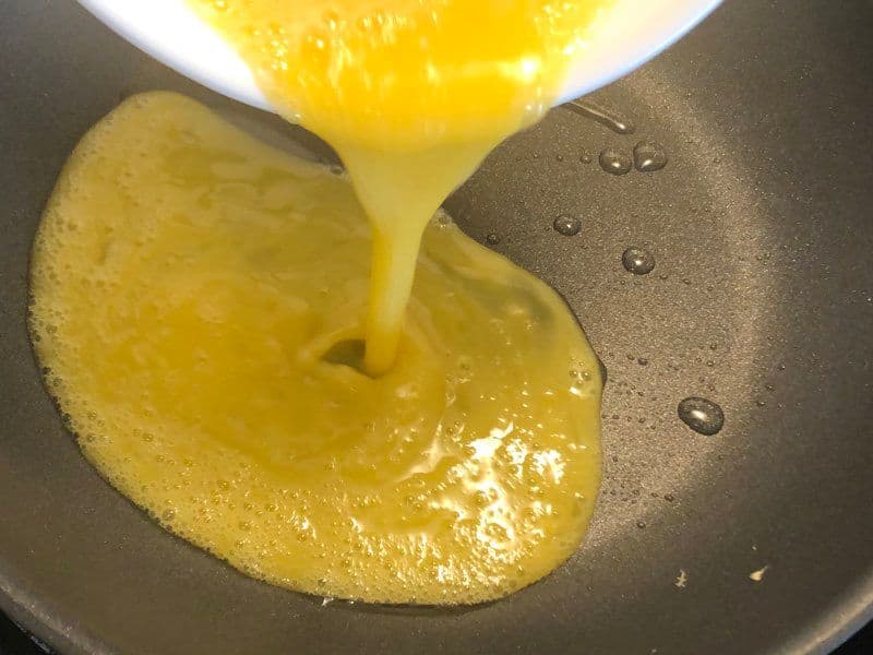 Whisked eggs being poured onto a hot pan to cook for a kathi roll.