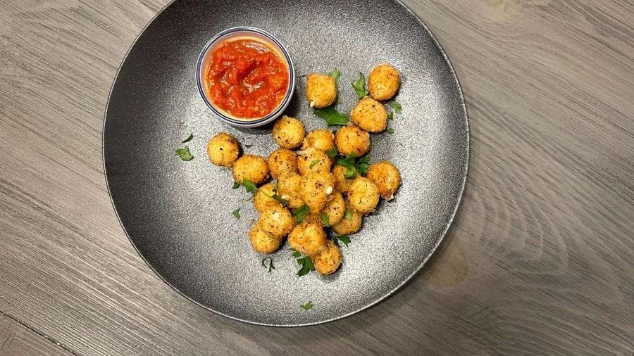 Golden-brown fried mozzarella balls on a gray plate with fresh herbs and red dipping sauce.