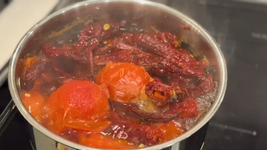 Saucepan with softened tomatoes and dried red chillies simmering in water for spicy momos chutney.